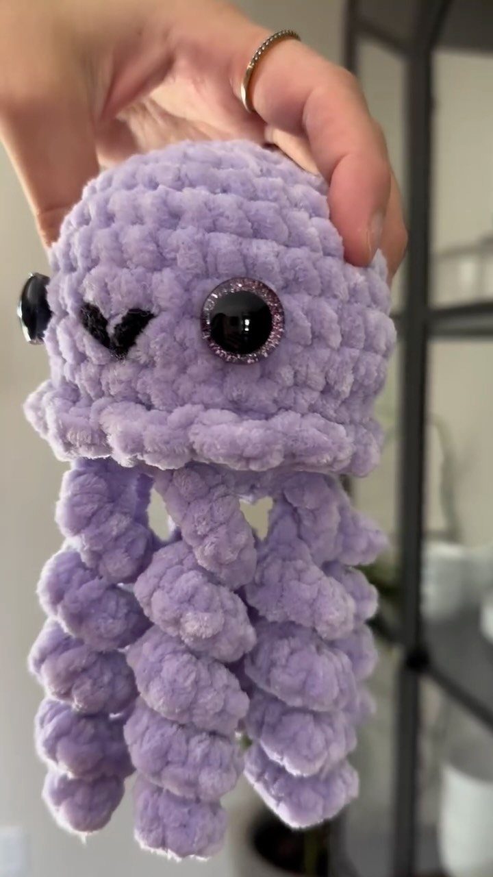 Purple crocheted jellyfish plushie held by a hand with a gold ring.