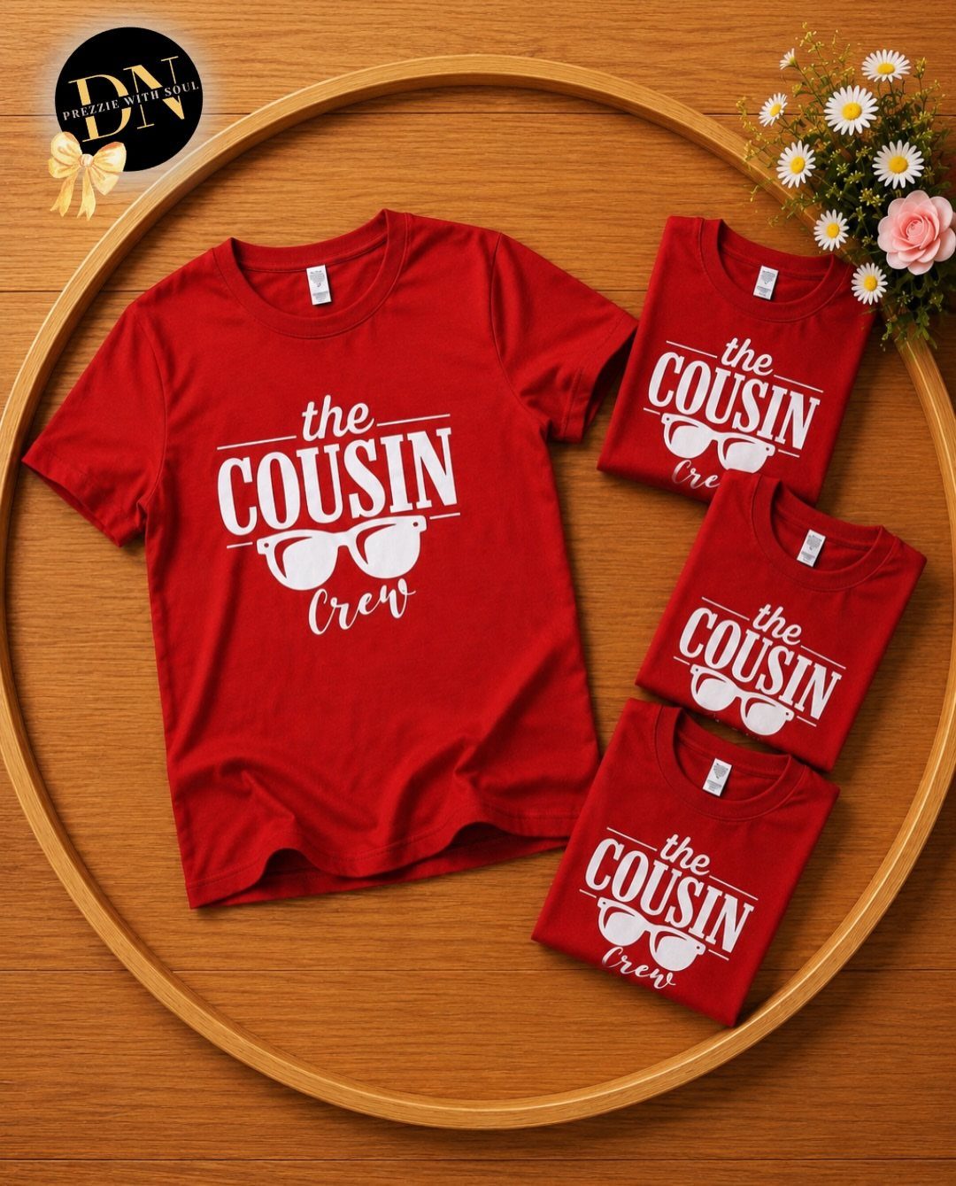 Four red t-shirts with white Cousin Crew text and sunglasses graphic on wood.