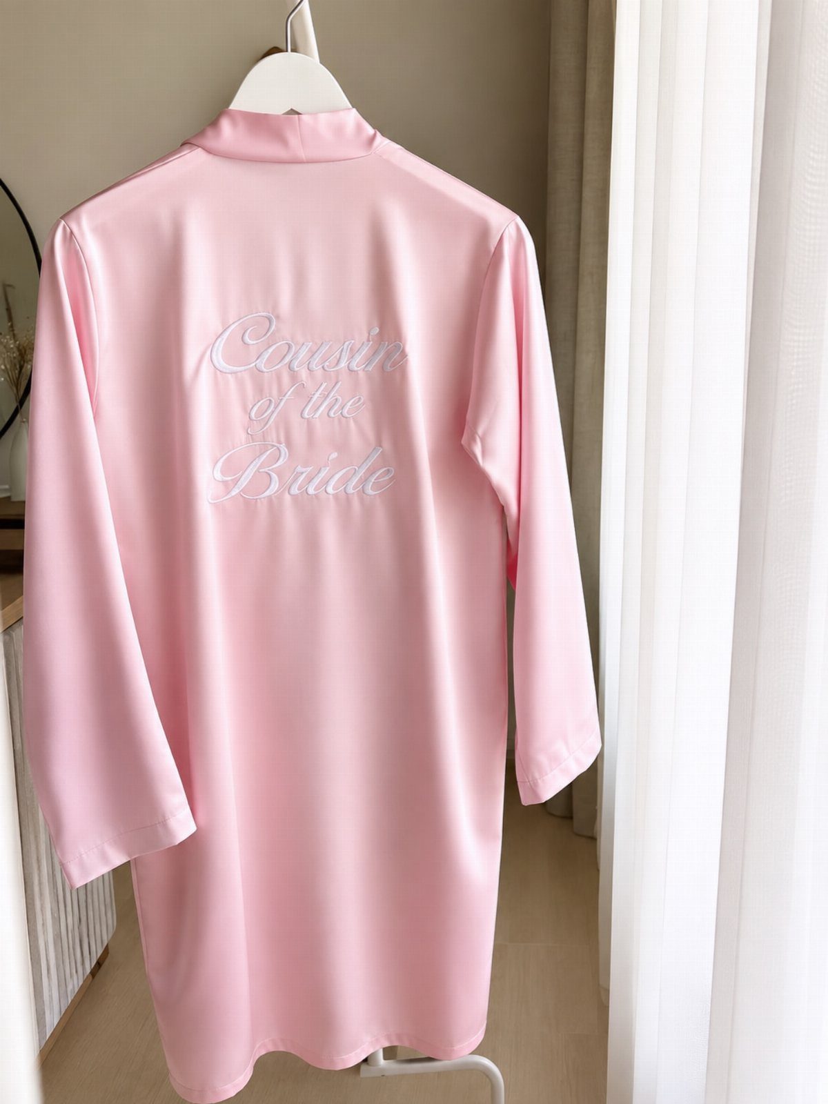 Pink satin bathrobe with Cousin of the Bride text hanging on a white hanger