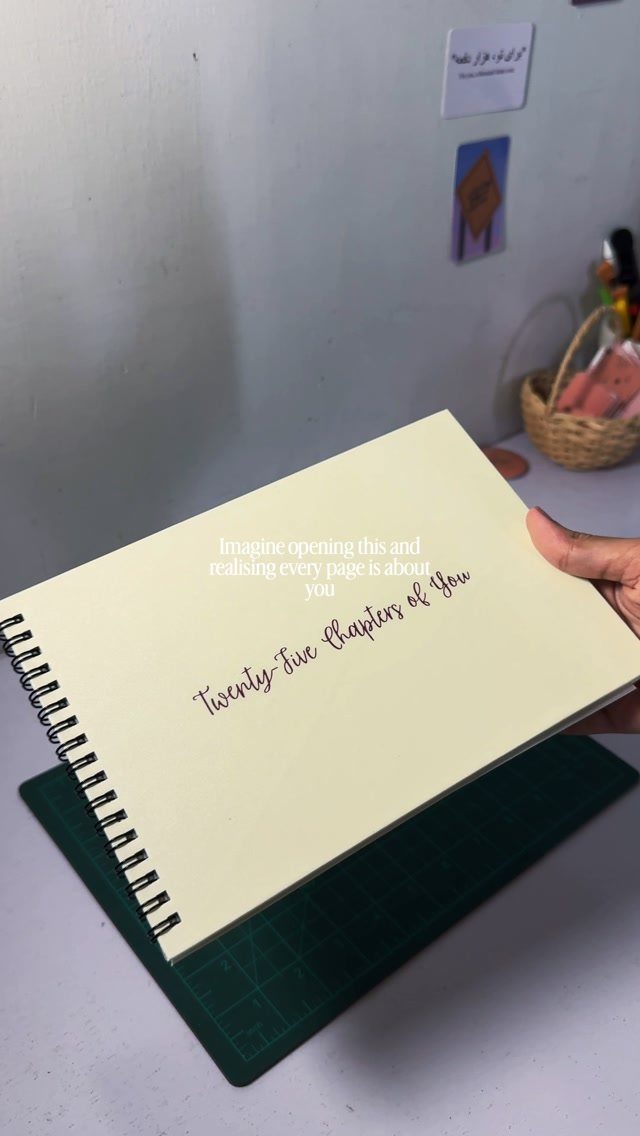 Cream spiral journal with cursive text held over a green cutting mat.