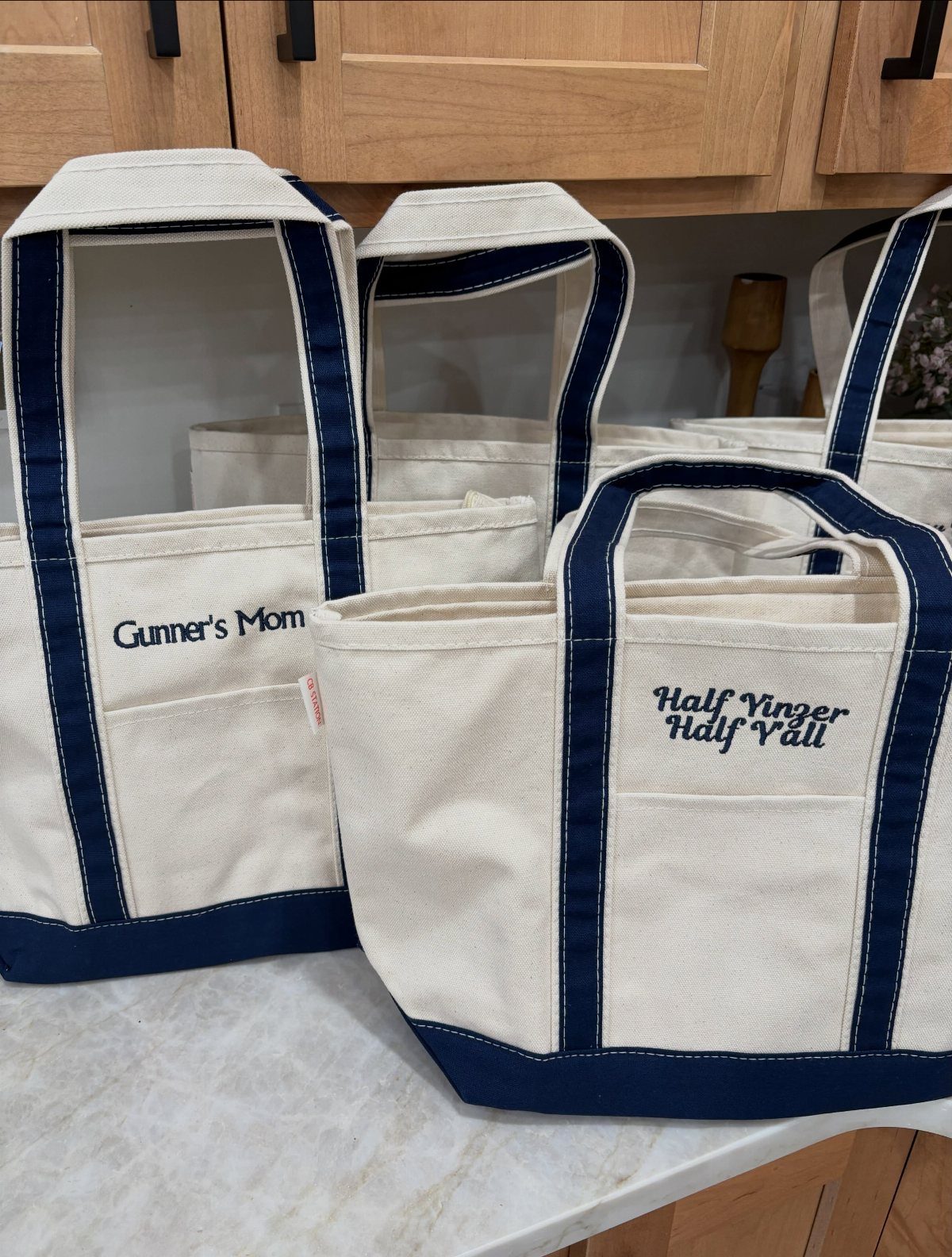 Cream canvas tote bags with navy blue accents and personalized embroidered text.