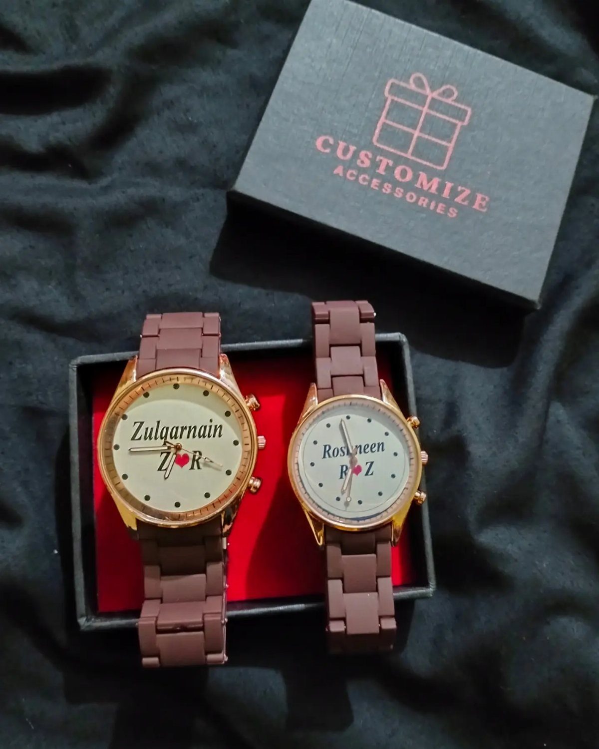 Two brown personalized wristwatches with custom names in a red-lined gift box.
