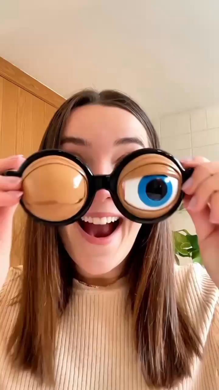 Woman wearing oversized novelty cartoon eye glasses and smiling in a bright room.