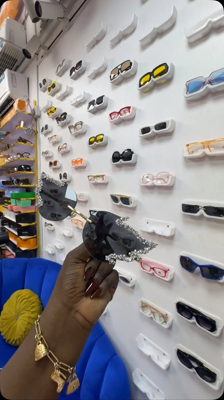 Heart-shaped black sunglasses with glittery edges held against a wall of eyewear.