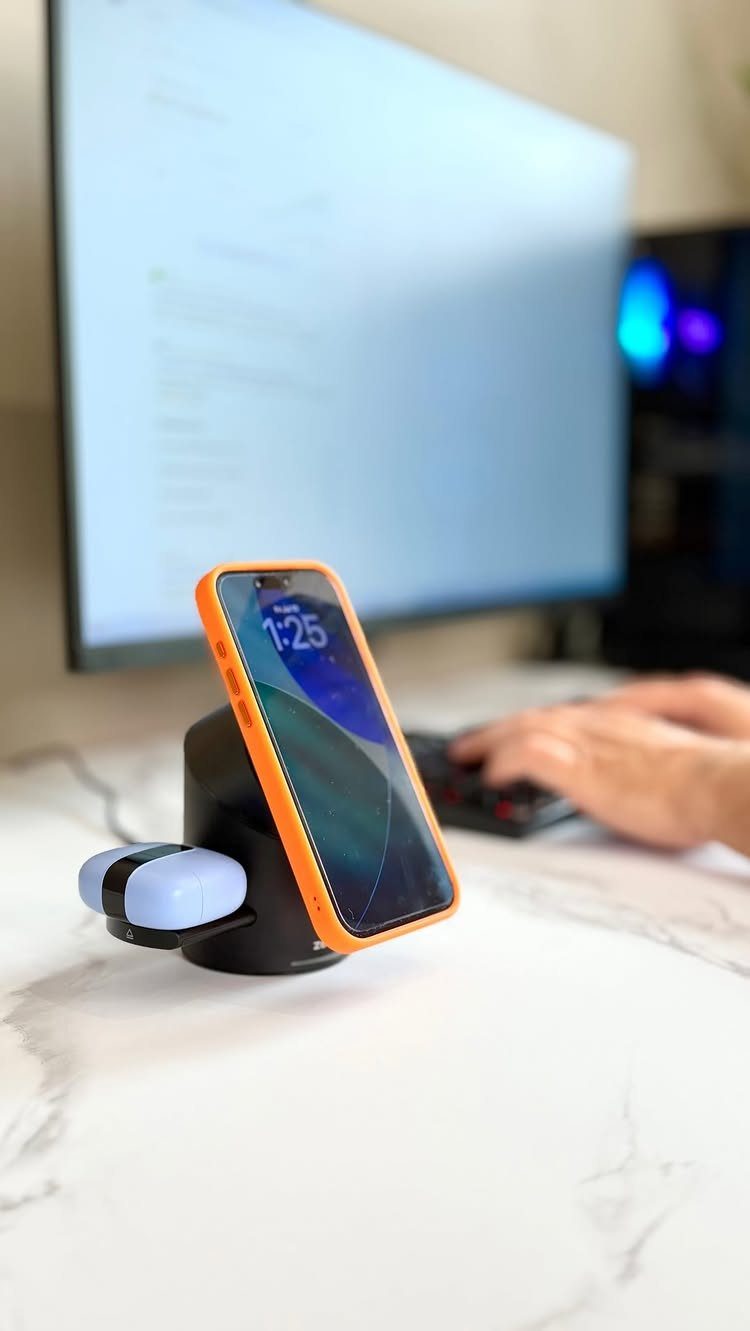 Wireless charging station holding a smartphone and earbuds on a white marble desk.