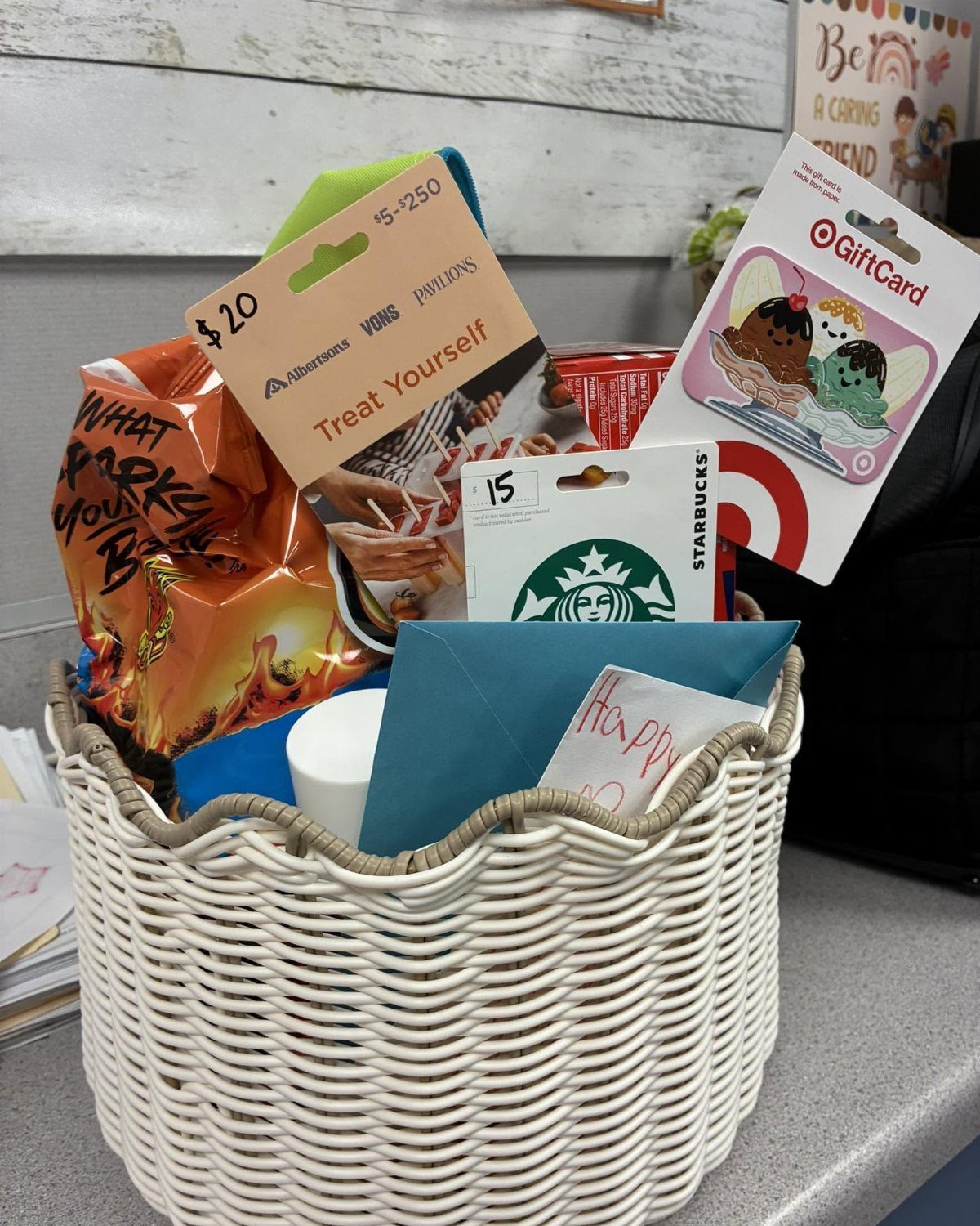 White woven gift basket containing various gift cards, snacks, and a blue envelope.