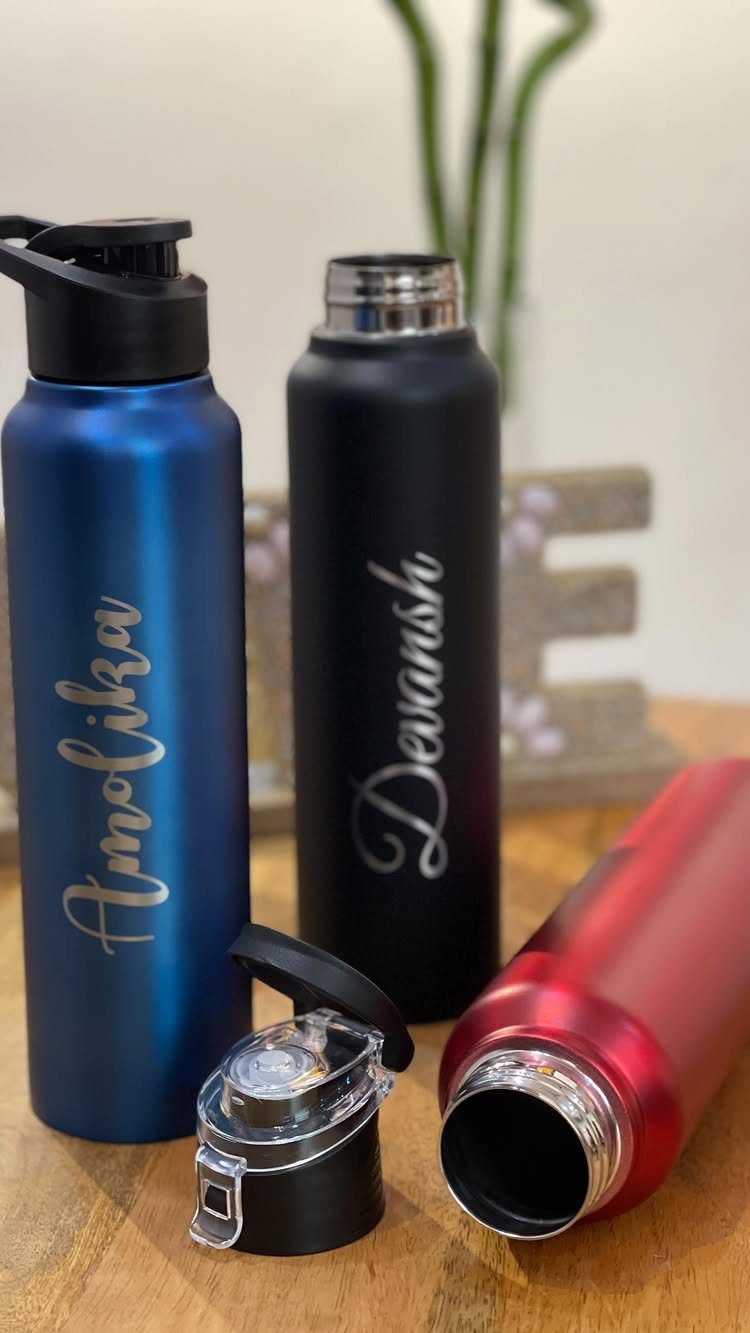Three personalized metal water bottles in blue, black, and red on wooden table
