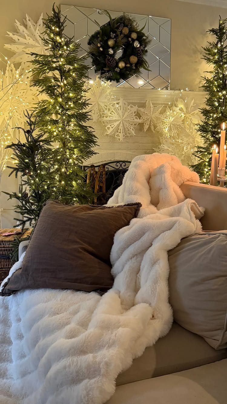 White faux-fur blanket and brown pillow on a sofa with Christmas trees behind.