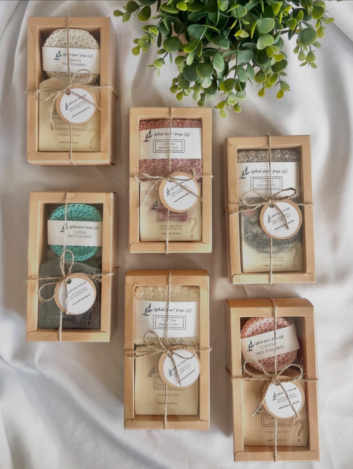 Six wooden spa gift boxes with soap and sponges on white fabric.