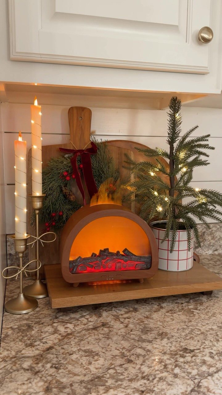 Small decorative electric fireplace with glowing embers, candles, and a miniature pine tree.