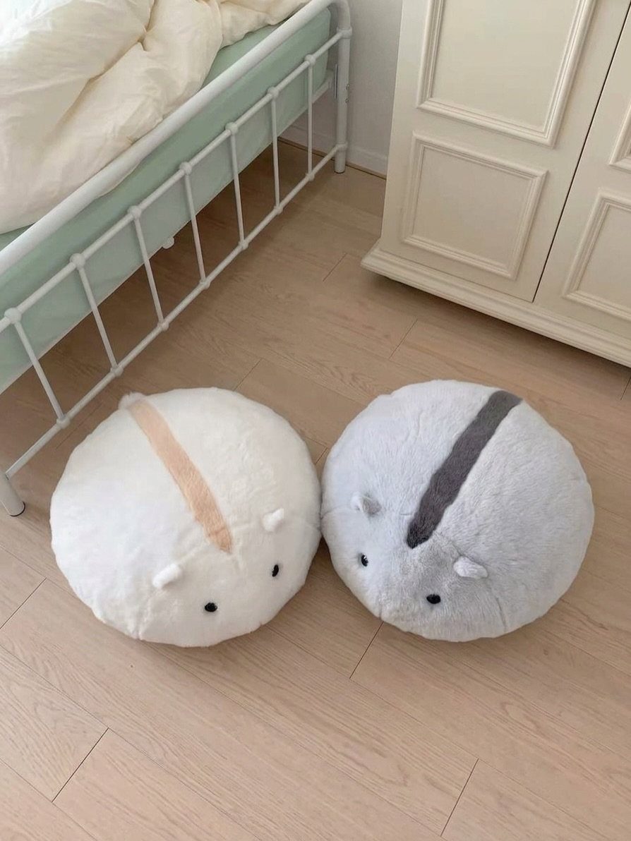 Two round fluffy plush toys sitting on a light wooden floor in a bedroom.