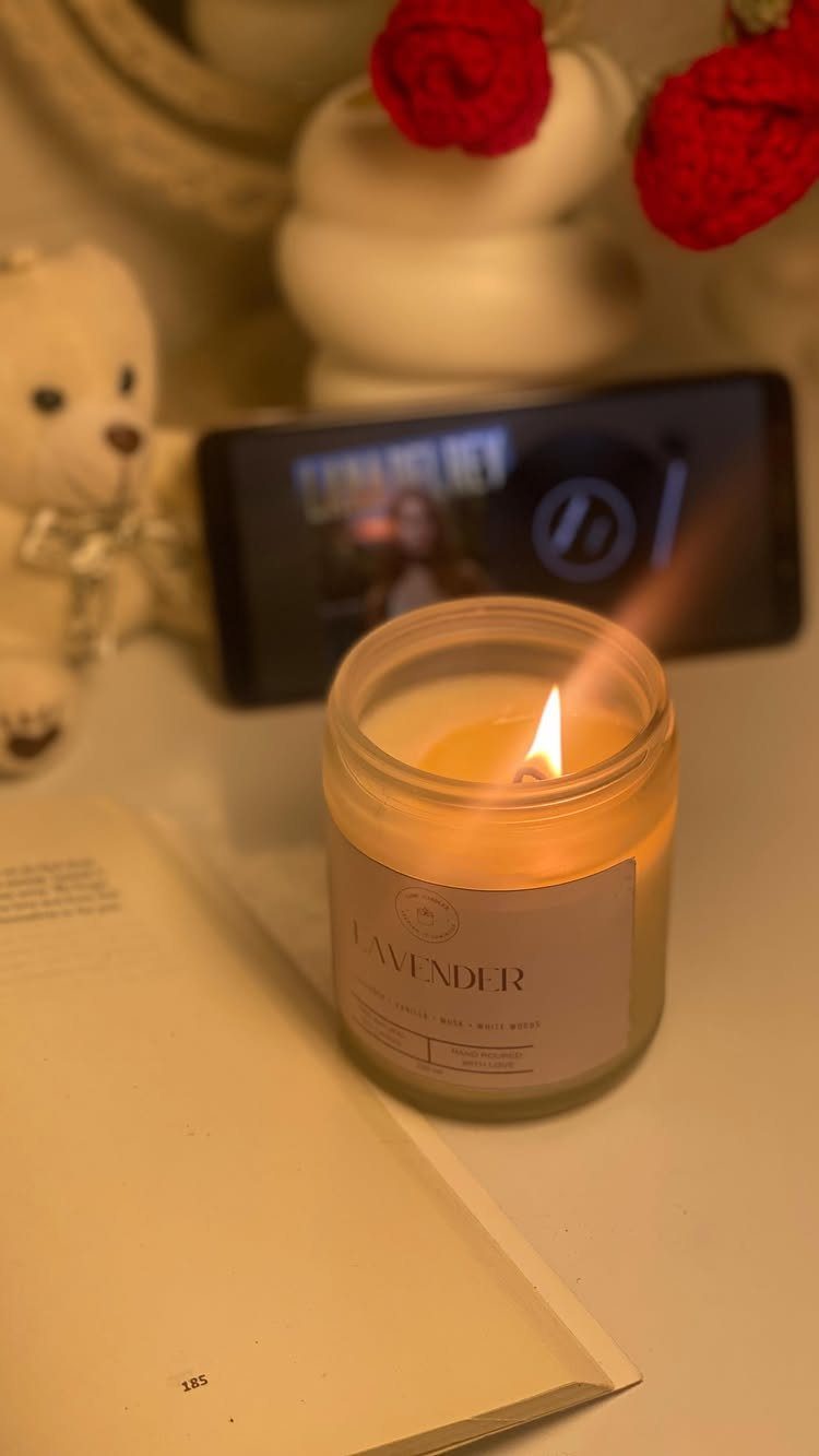 Lit lavender scented candle in a glass jar next to an open book.