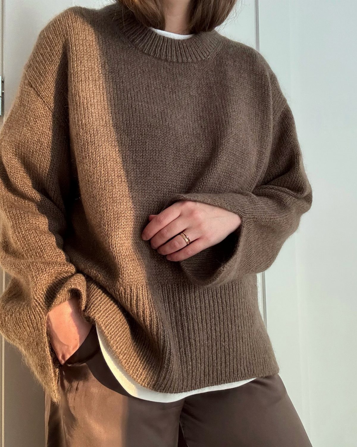 Brown knit crewneck sweater worn over a white shirt and brown trousers.