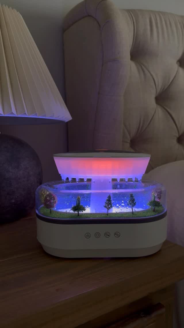 Essential oil diffuser with miniature landscape and colorful lights on a wooden nightstand.