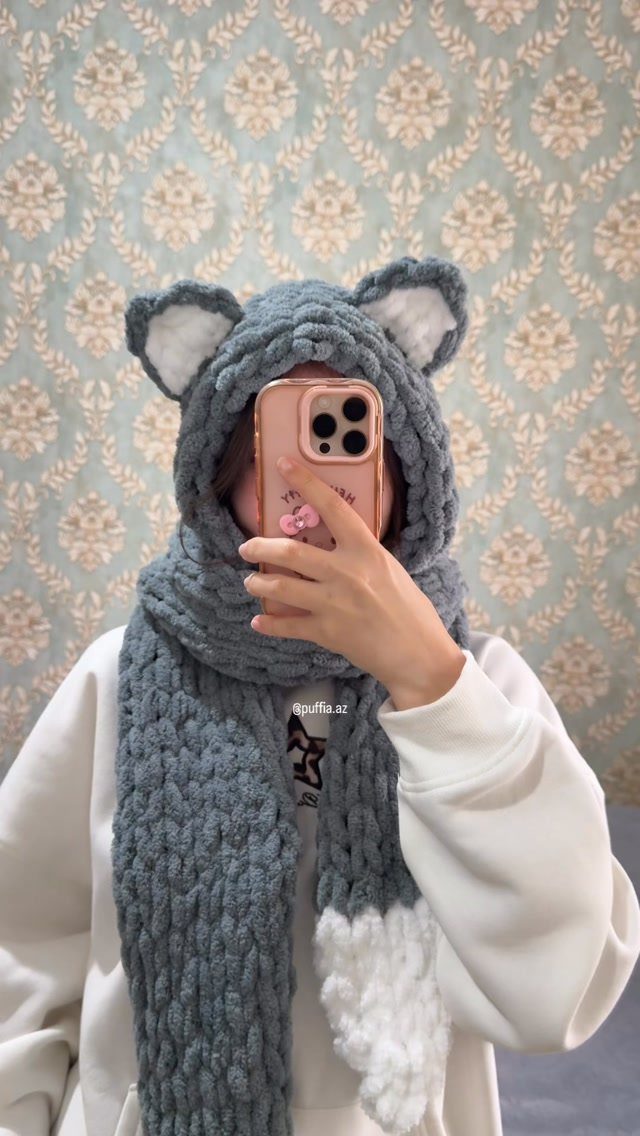 Person wearing a chunky grey knitted animal hood and matching long scarf.
