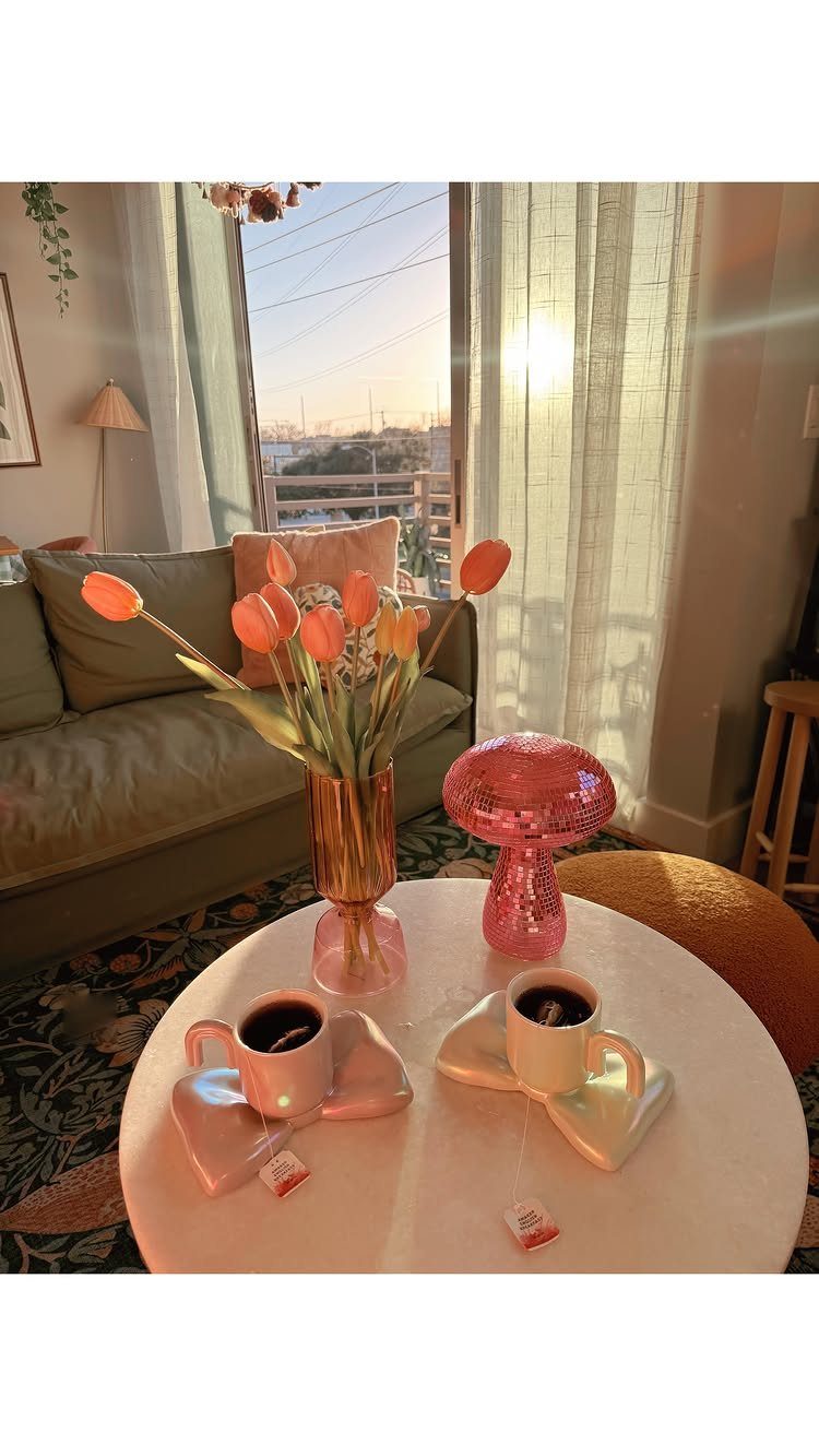 Two white coffee mugs on heart-shaped coasters next to orange tulips and a lamp.
