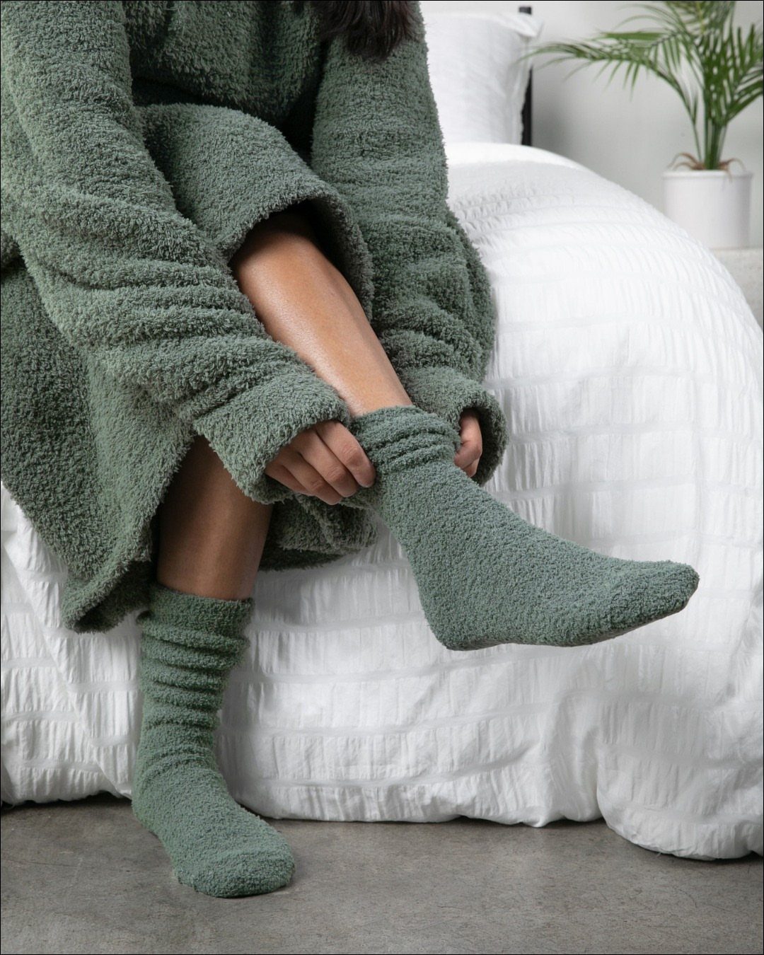 Person wearing a fuzzy olive green robe and matching socks on a white bed