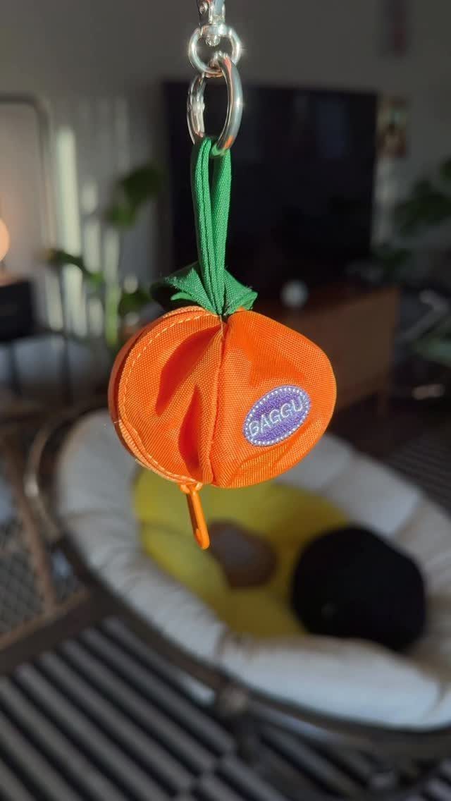 Orange pumpkin-shaped Baggu bag charm hanging from a silver metal clip.
