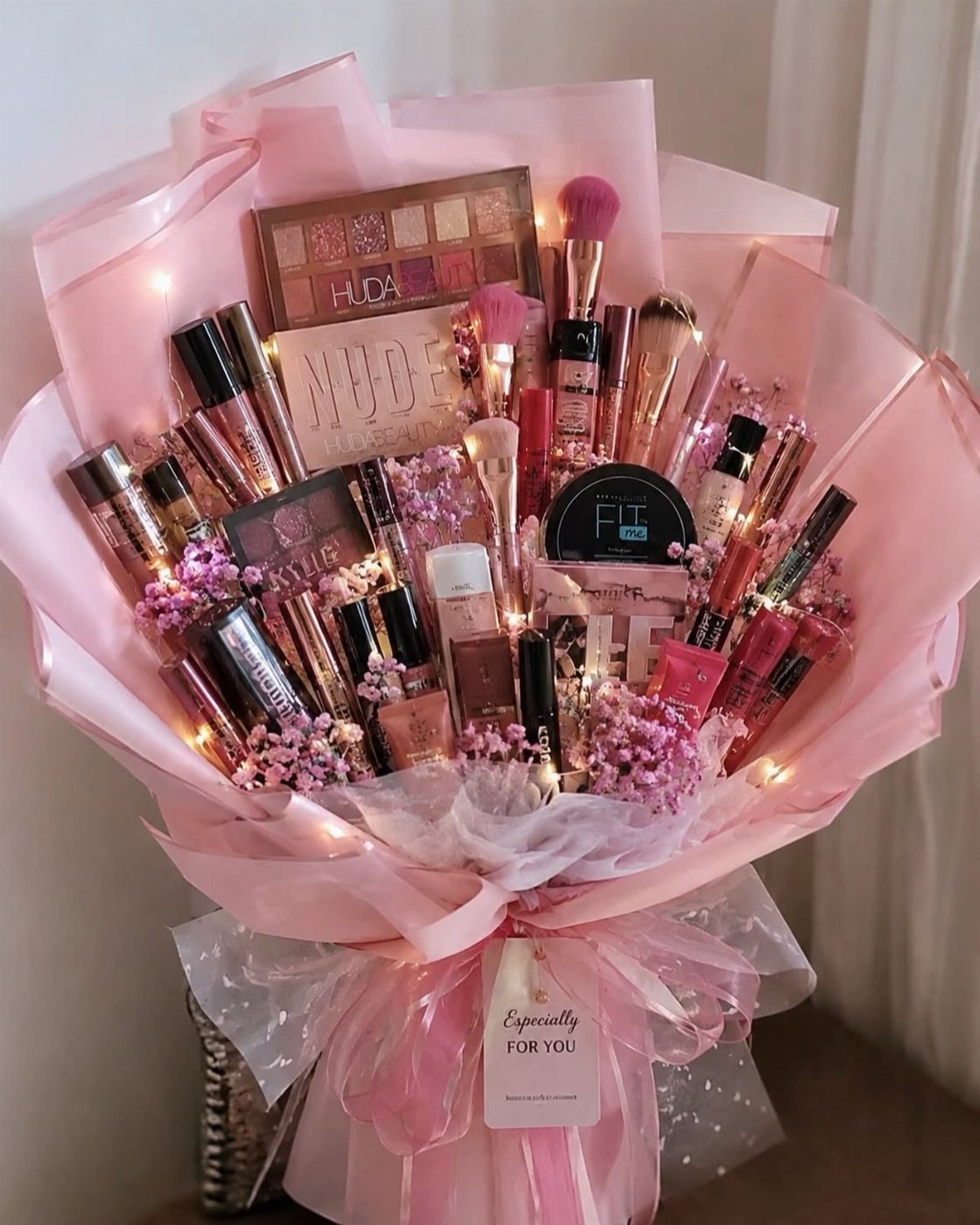 Makeup bouquet with eyeshadows, lip glosses, and pink flowers wrapped in pink paper.