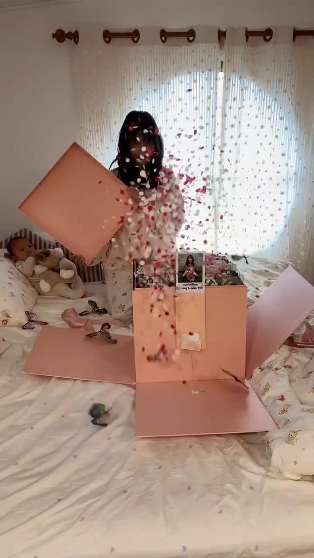 Person opening a pink explosion gift box with confetti flying on a bed