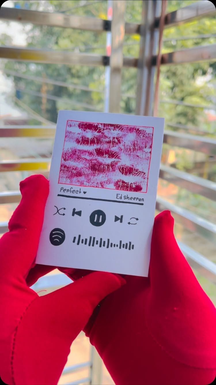 White card with lip prints and Spotify code held by red gloved hands.