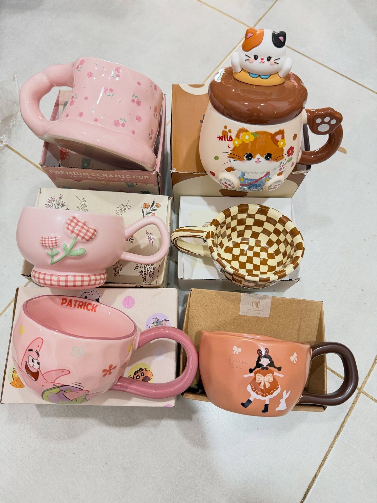 Six cute decorative ceramic mugs with animal illustrations on a tiled floor.