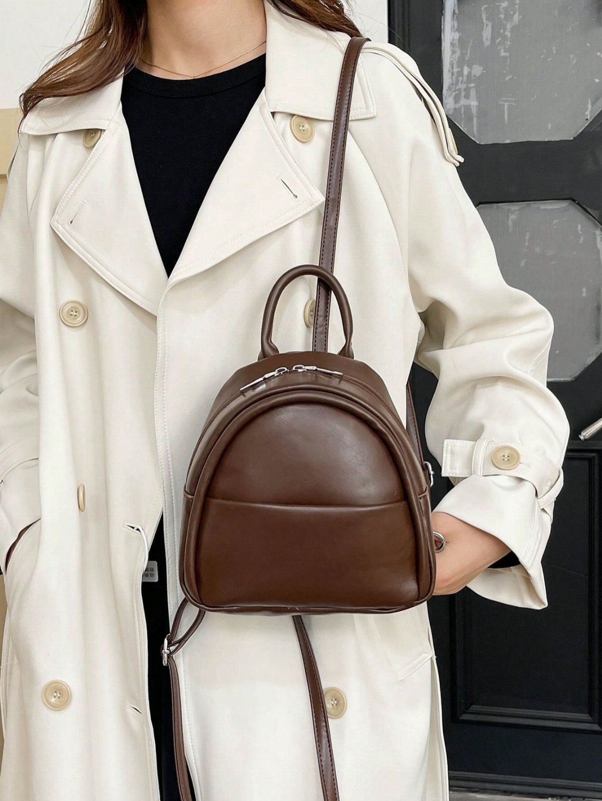 Brown leather mini backpack worn by a person in a white trench coat.