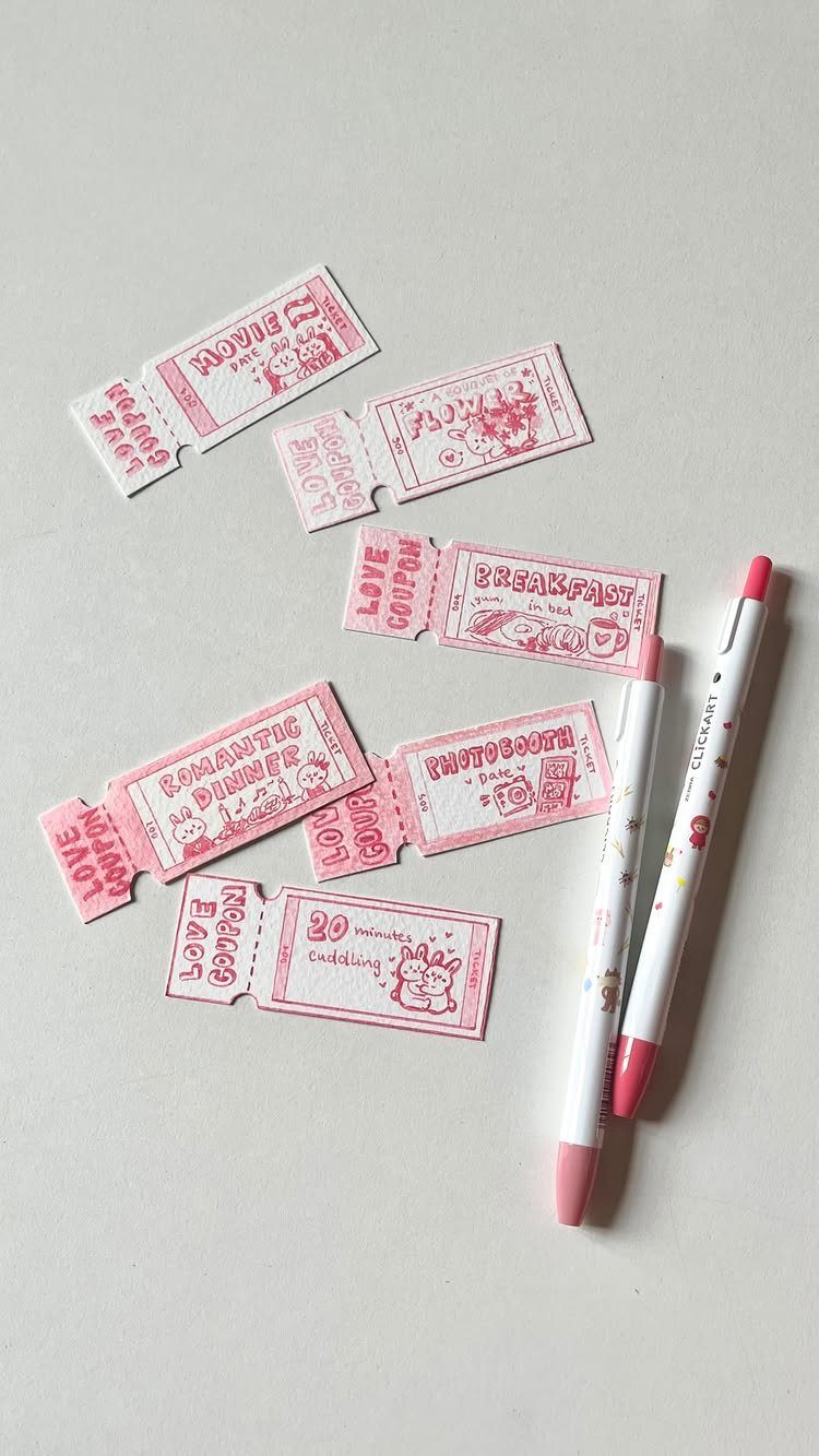Handmade pink love coupons and markers scattered on a light grey background.