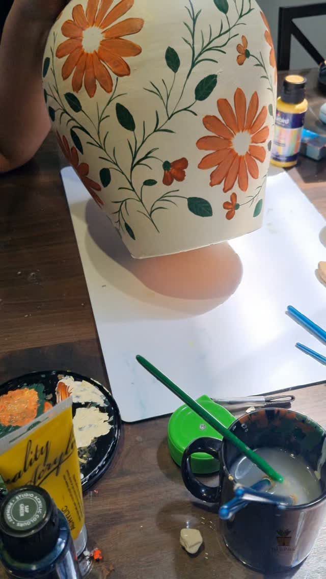 Hand-painted cream vase with orange flowers and green leaves on a wooden table.