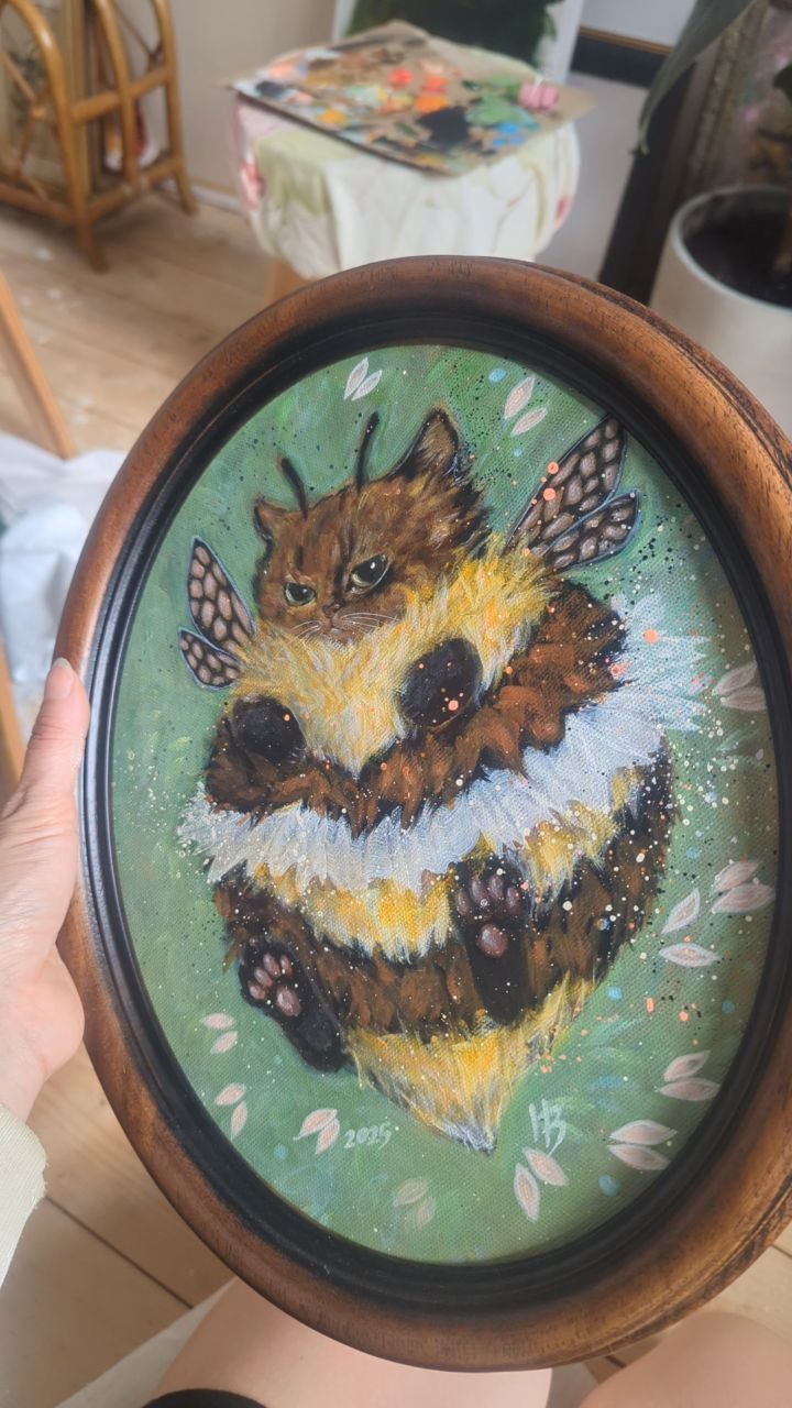 Oval framed painting of a fluffy brown cat dressed as a bumblebee.