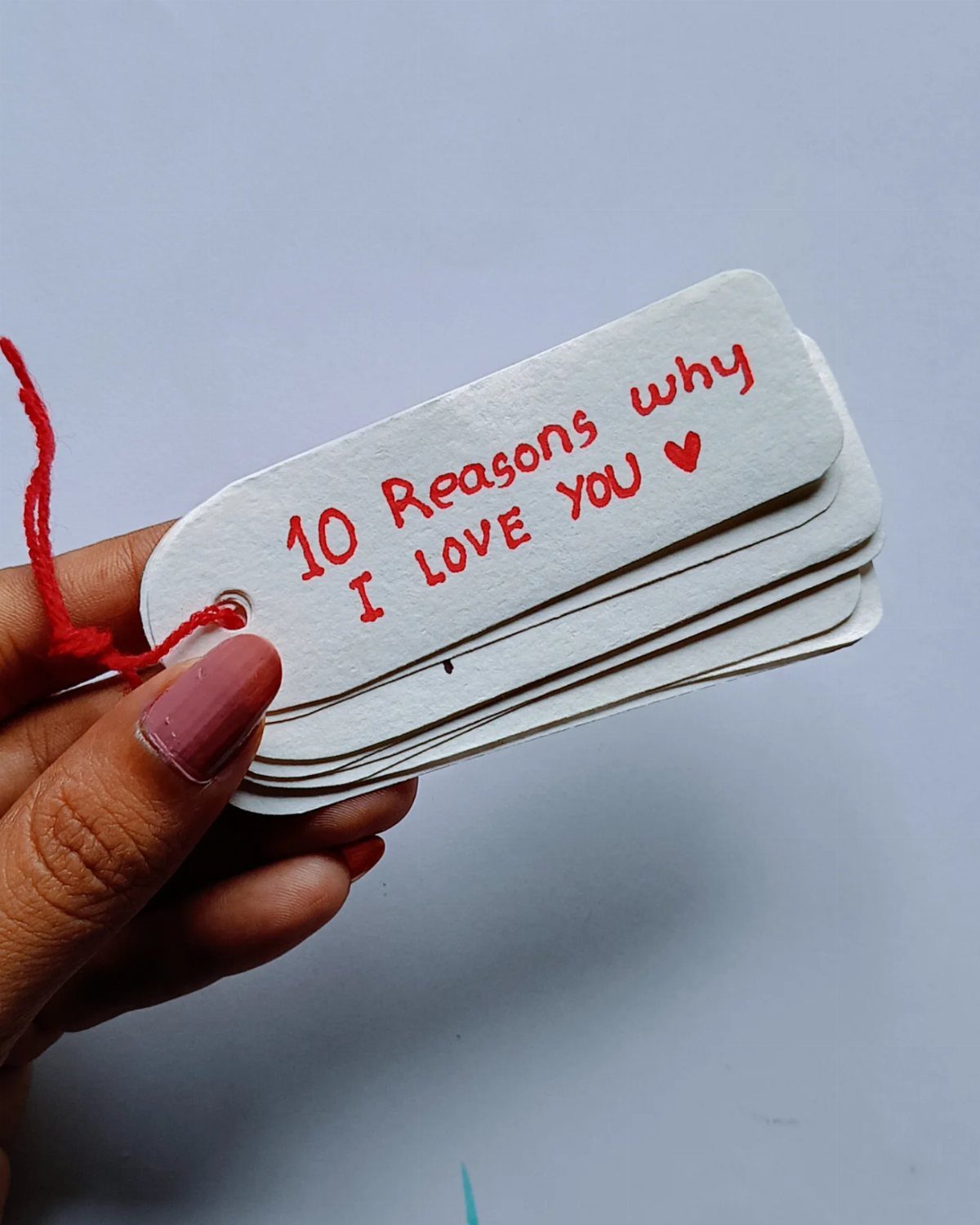 Hand holding a stack of white tags with handwritten red love notes.