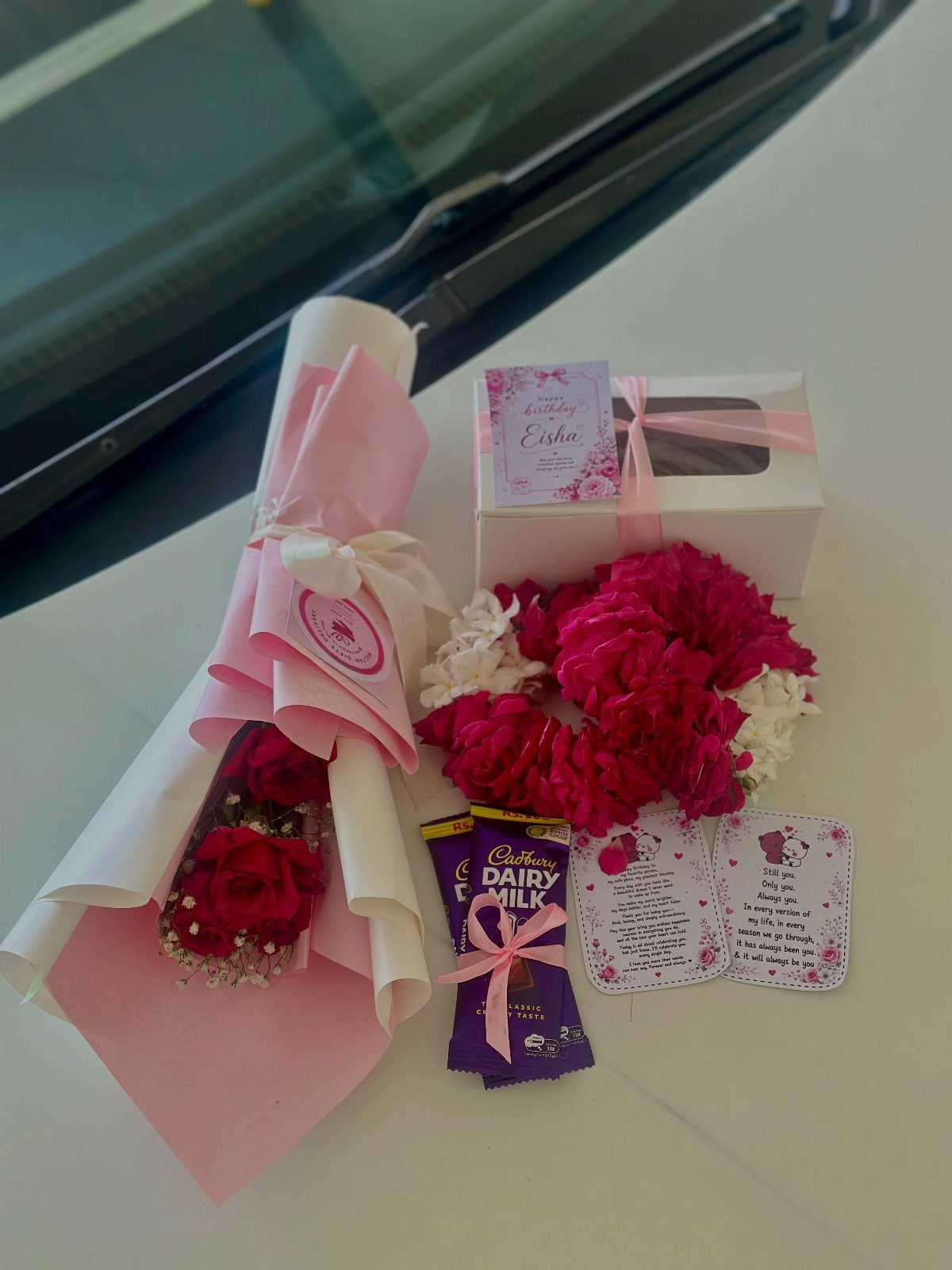 Gift set with red roses, chocolates, a white gift box, and a handwritten note.