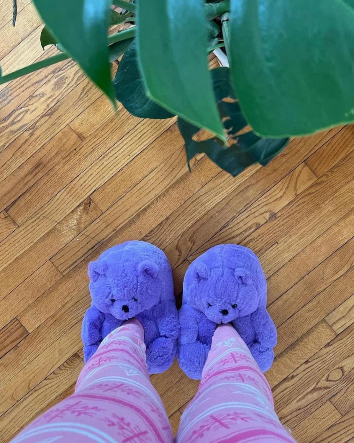 Purple teddy bear plush slippers and pink striped pajama pants on wooden floor