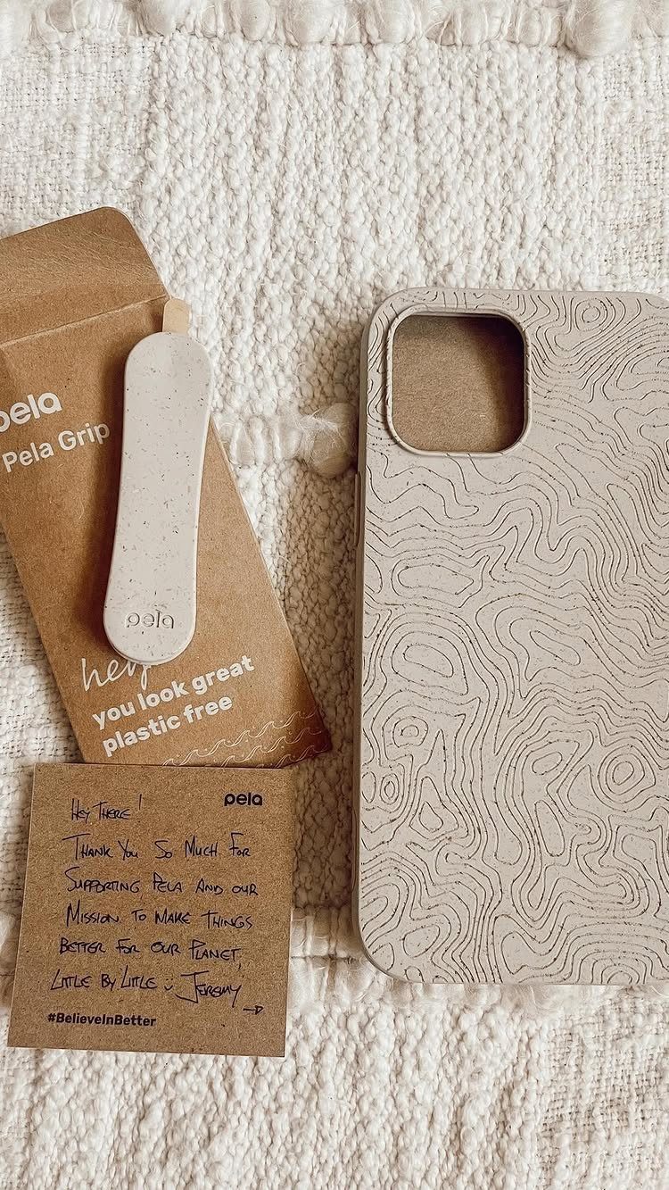 Beige patterned phone case and grip with cardboard packaging on white fabric.