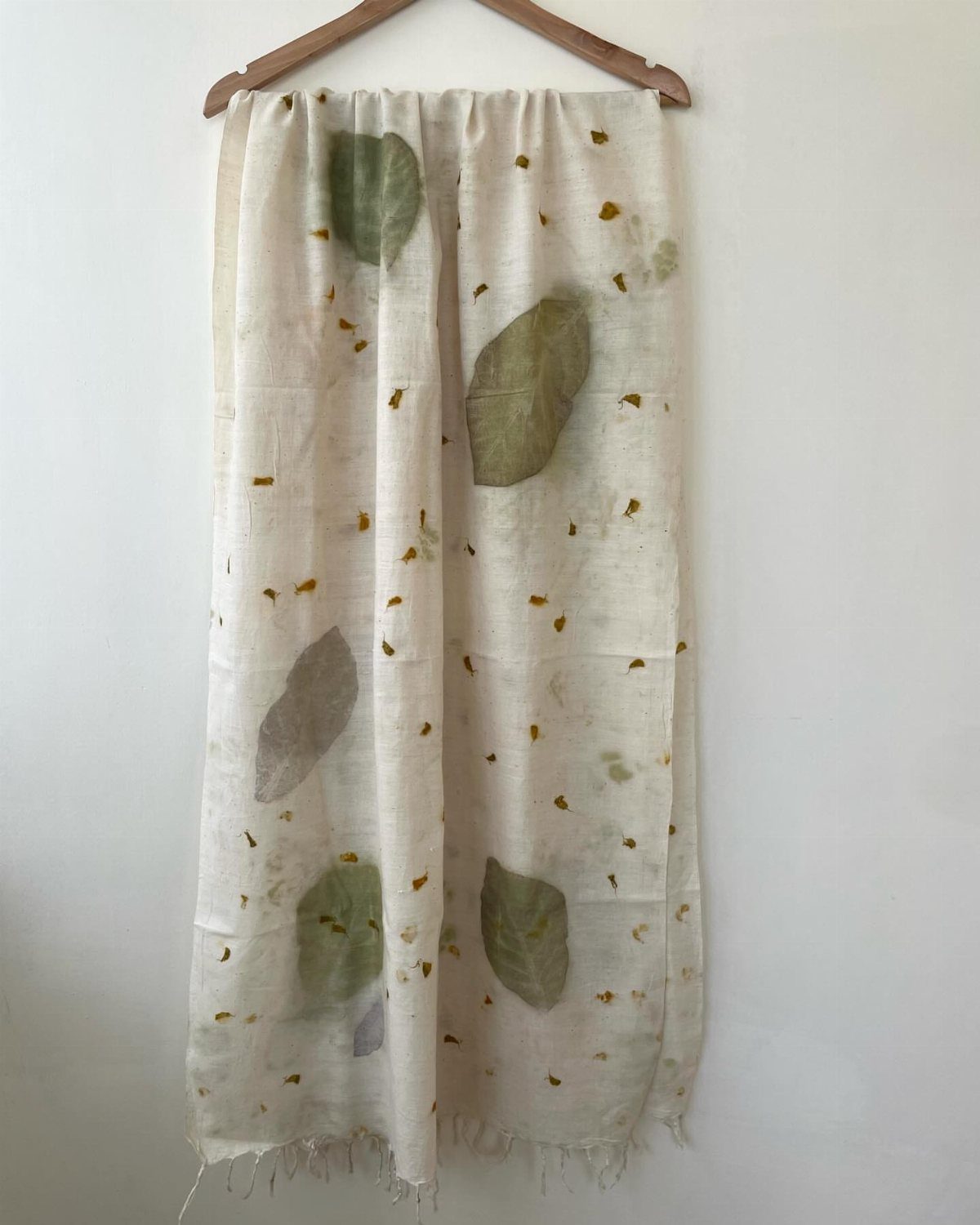 White fabric scarf with green leaf prints hanging on a wooden hanger