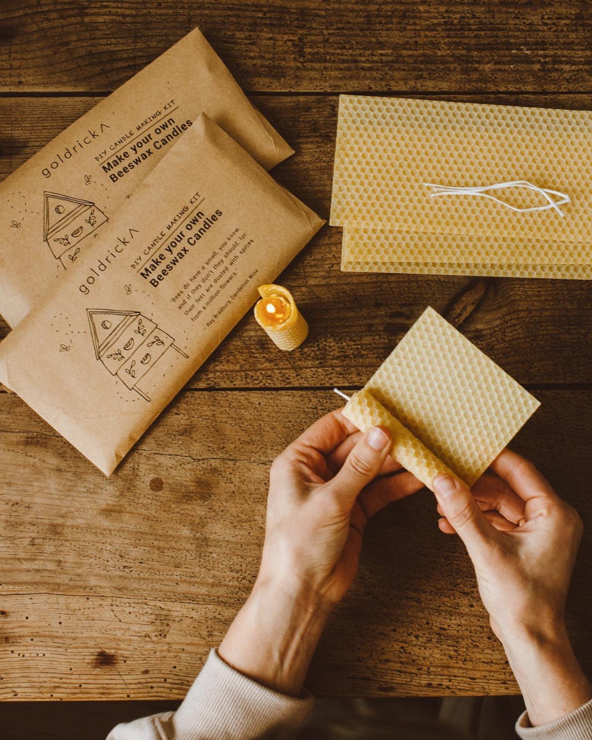 Hands rolling a yellow beeswax sheet into a candle on a wooden table.