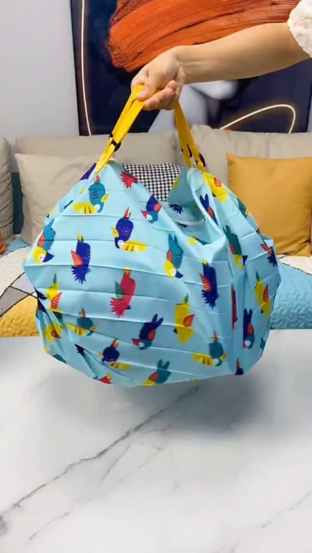 Light blue reusable grocery bag with yellow handles and colorful bird patterns.