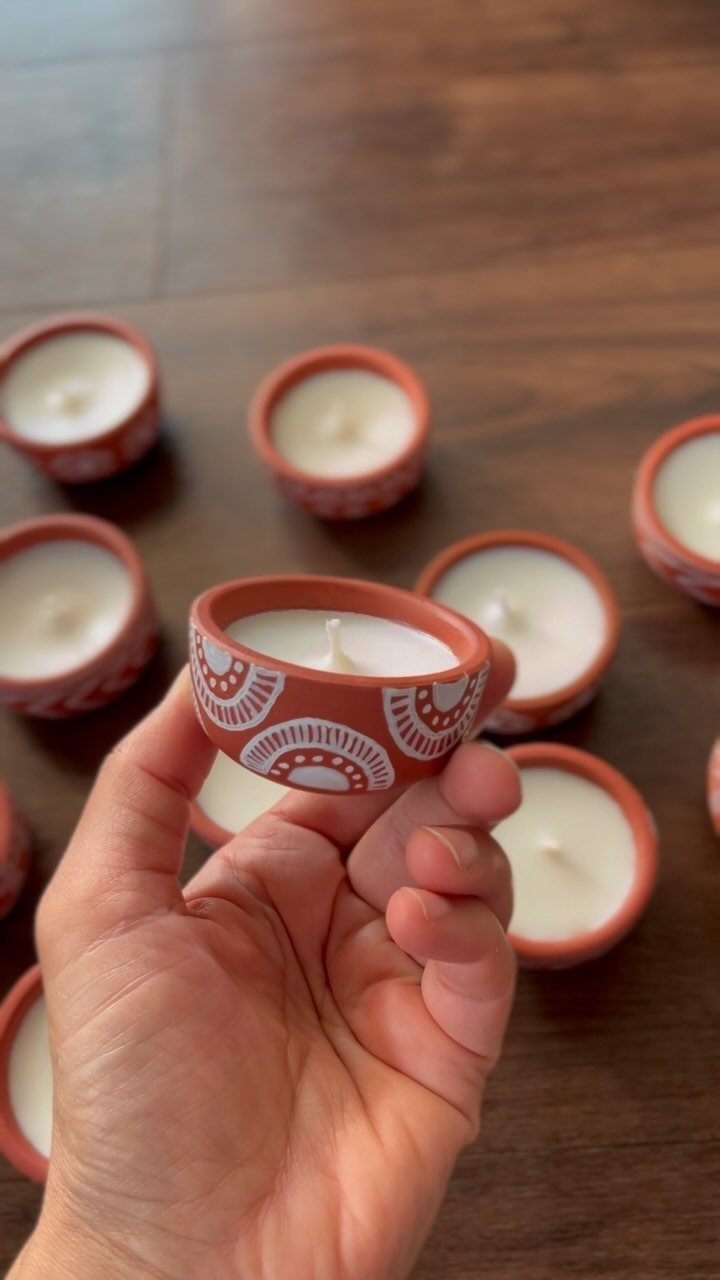 Hand holding a decorative terracotta candle holder among others on a wooden table