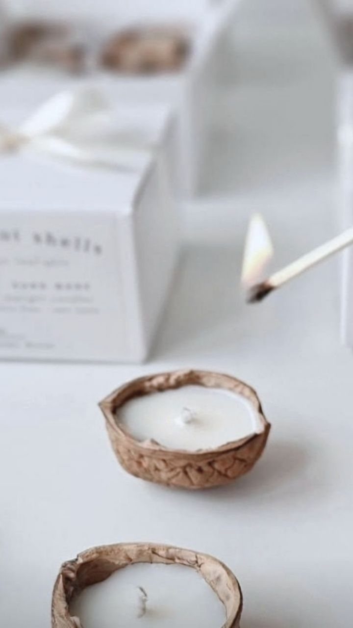 White candles in walnut shells with a gift box and lit match.