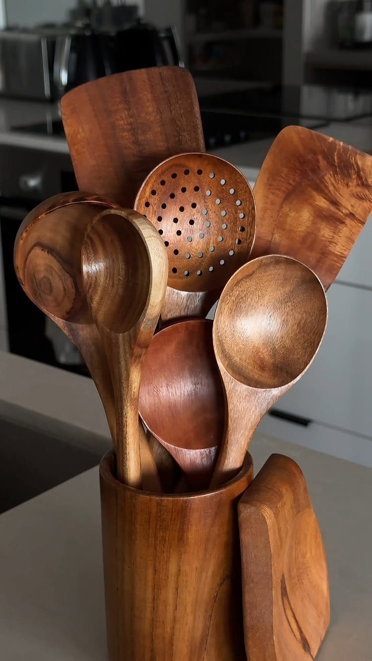Wooden kitchen utensils and spoons stored in a matching wooden holder on a counter.