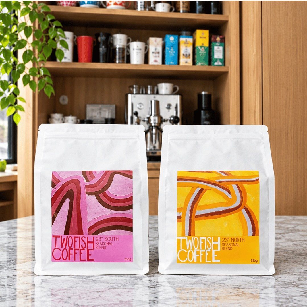 Two white bags of artisanal coffee with colorful labels on a marble counter.