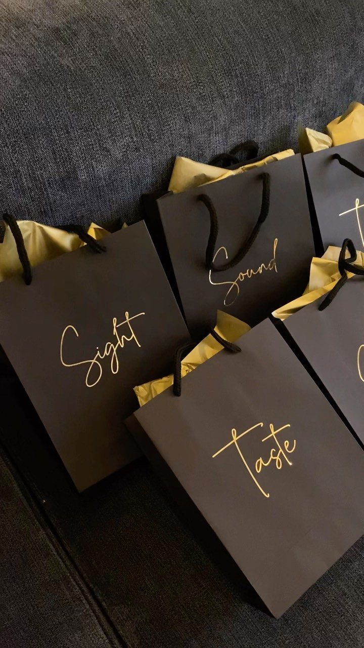 Black gift bags with gold lettering for sight, sound, and taste on grey fabric