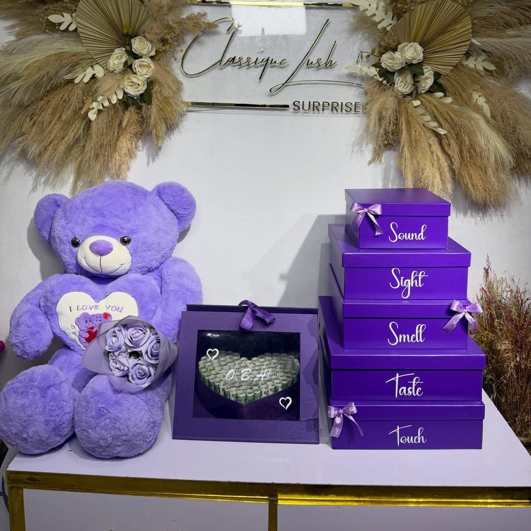 Purple teddy bear and five stacked purple gift boxes labeled with the five senses.