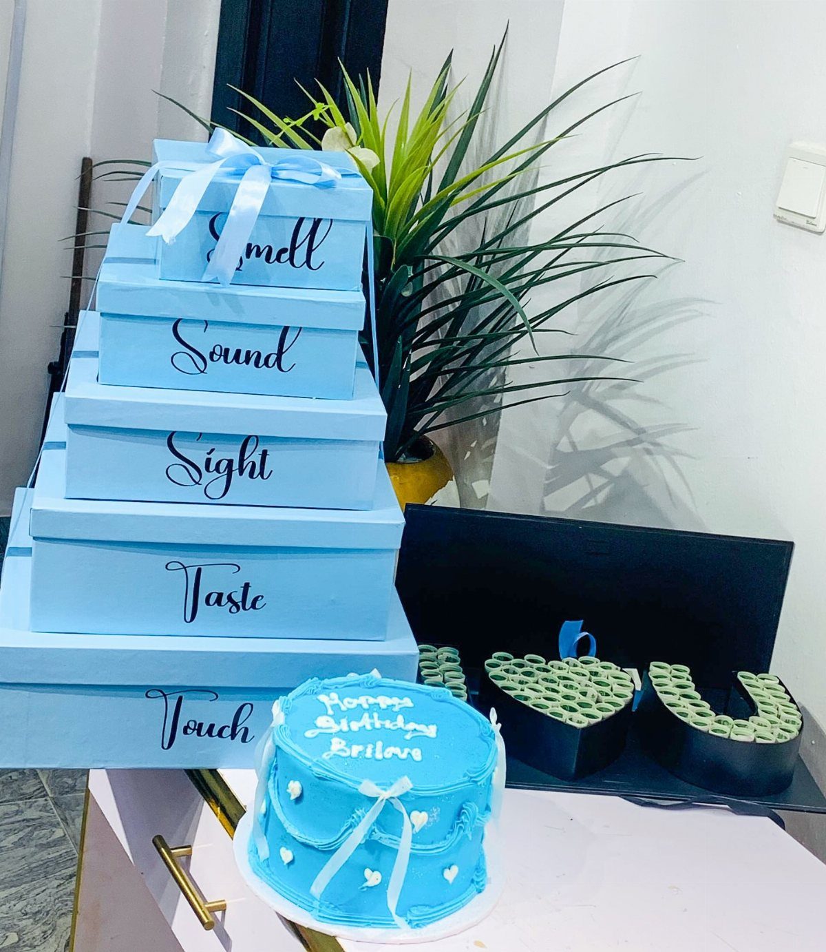 Stacked blue gift boxes labeled with the five senses next to a blue cake.