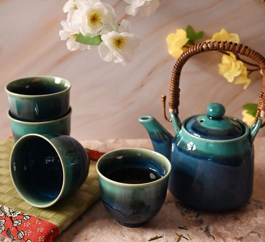 Teal ceramic tea set with teapot and cups on a marble surface.