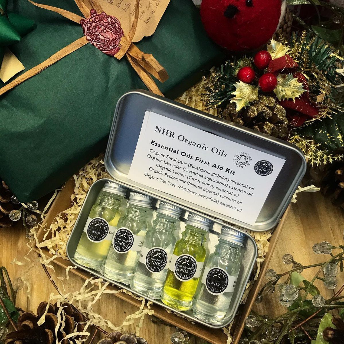 Essential oil kit in a metal tin surrounded by festive holiday decorations.
