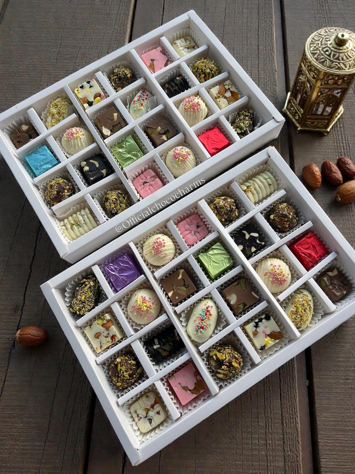 Assorted gourmet chocolates in two white gift boxes on a wooden table.