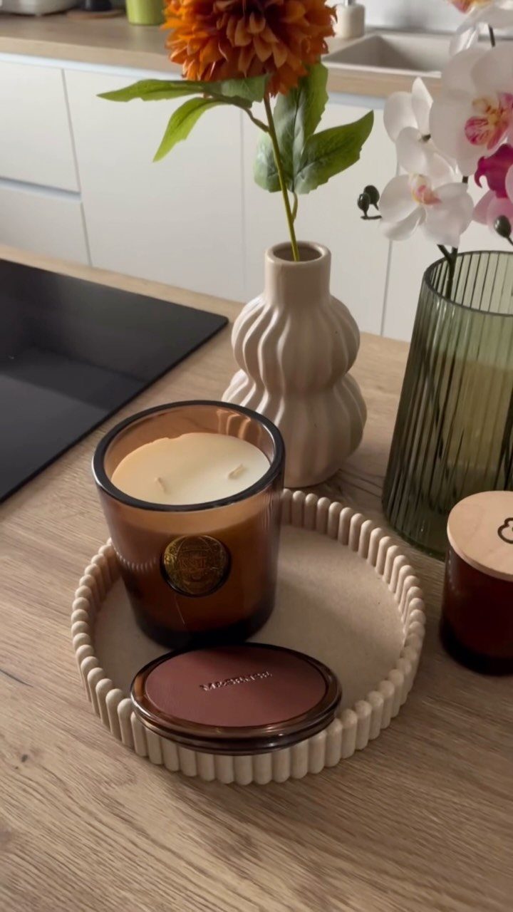 Brown glass scented candle sitting in a ribbed cream tray on wooden counter