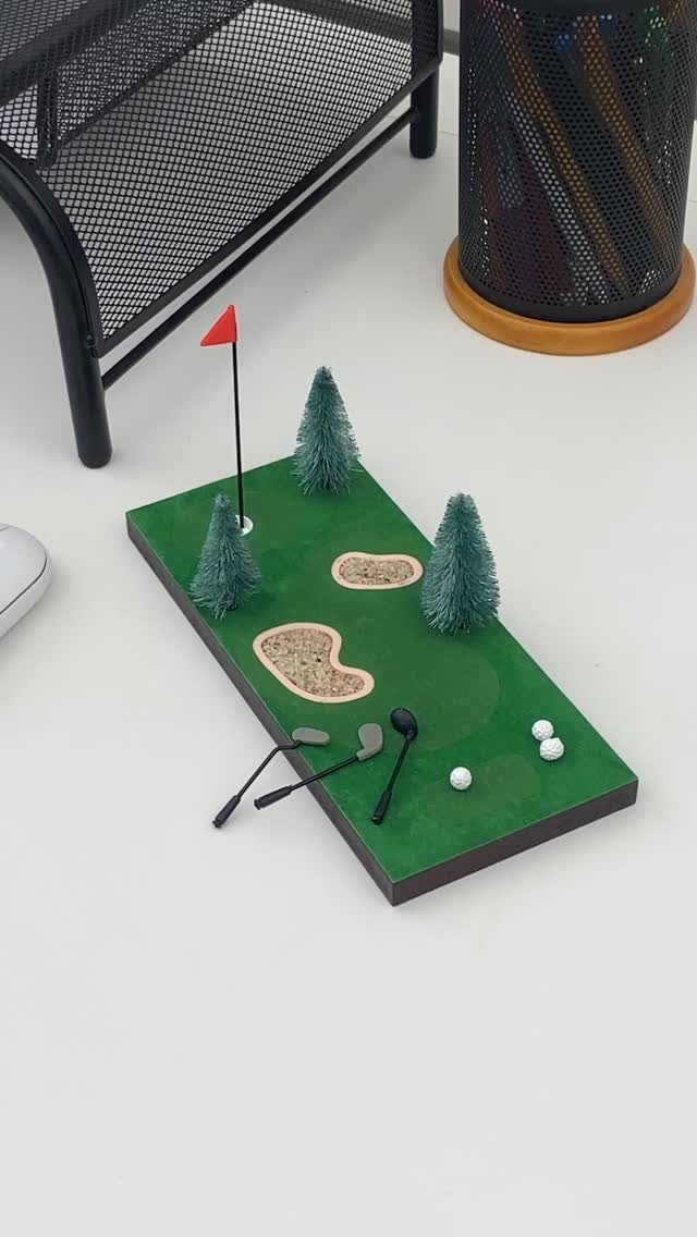 Miniature golf putting green with tiny trees and putters on a white desk