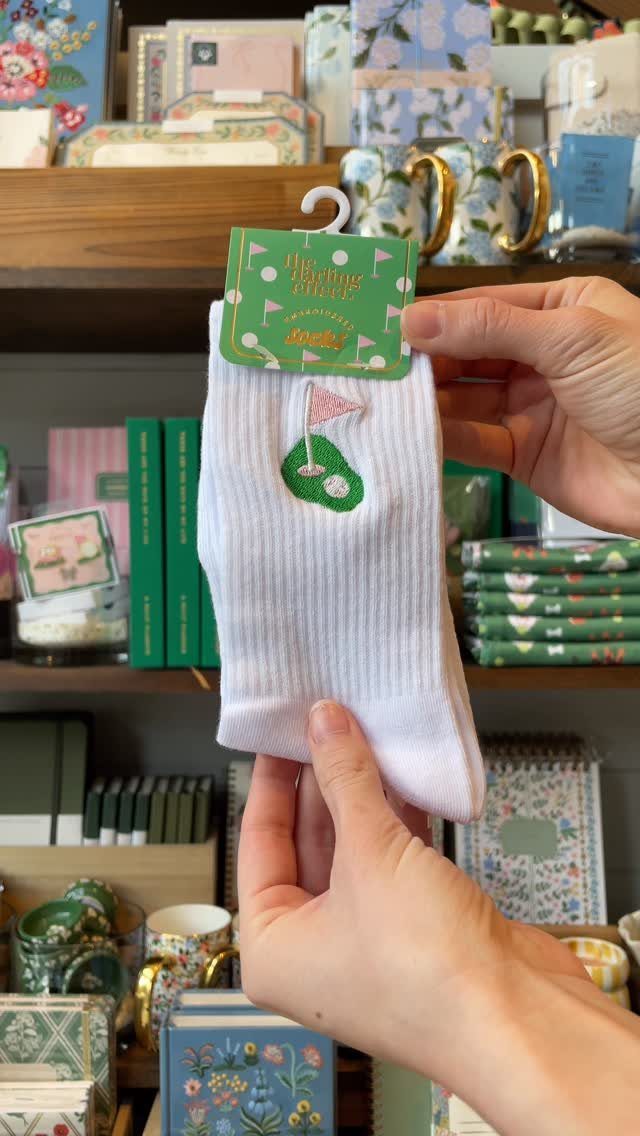 White ribbed sock with embroidered golf green held by hands in a shop